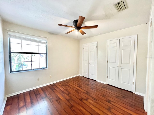 unfurnished bedroom with ceiling fan, multiple closets, and dark hardwood / wood-style floors