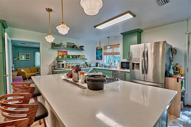 kitchen with a center island, sink, hanging light fixtures, green cabinets, and appliances with stainless steel finishes