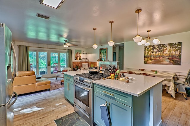 kitchen with appliances with stainless steel finishes, hanging light fixtures, ceiling fan with notable chandelier, light wood-type flooring, and a center island