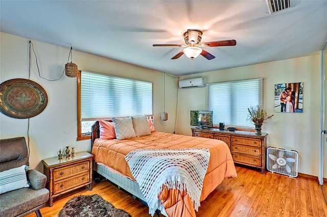 bedroom featuring multiple windows, light wood-type flooring, an AC wall unit, and ceiling fan