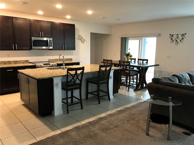 kitchen featuring appliances with stainless steel finishes, a kitchen breakfast bar, light stone counters, light tile patterned floors, and a center island with sink