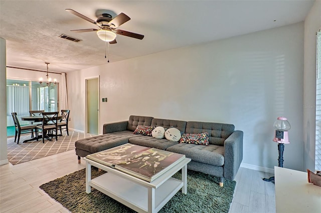 living room with light wood-type flooring, ceiling fan with notable chandelier, and a textured ceiling