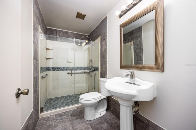 bathroom with tile walls, a shower with shower door, toilet, and tile patterned flooring