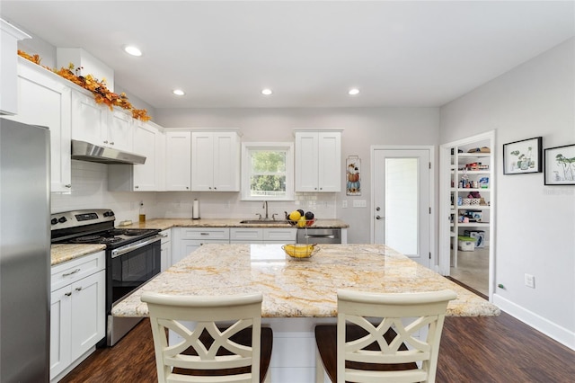 kitchen featuring light stone counters, dark wood-type flooring, white cabinetry, stainless steel appliances, and a center island