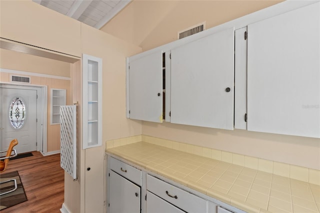 kitchen featuring white cabinets, tile counters, lofted ceiling with beams, and hardwood / wood-style floors