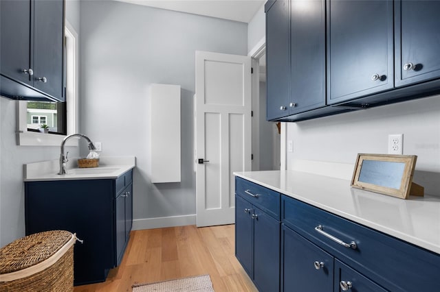 kitchen with blue cabinetry, a sink, light countertops, and light wood-type flooring