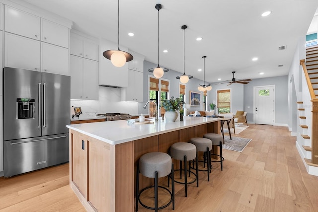 kitchen with a sink, light wood-style floors, high quality fridge, a center island with sink, and visible vents