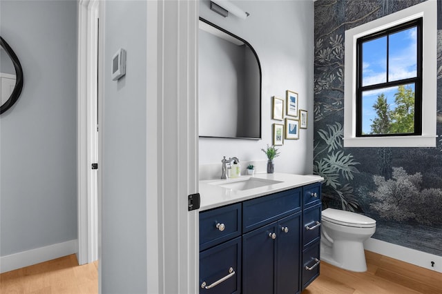 bathroom featuring wallpapered walls, wood finished floors, toilet, vanity, and baseboards