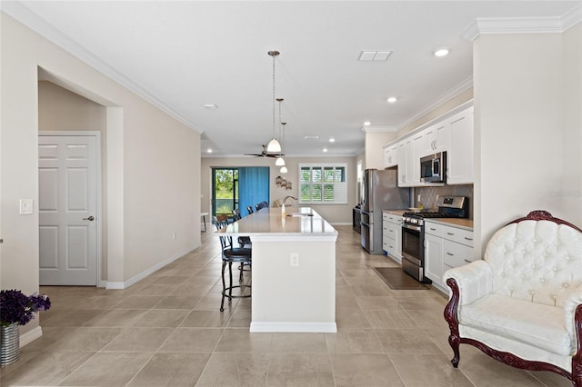 kitchen with ceiling fan, decorative light fixtures, a kitchen island with sink, white cabinetry, and appliances with stainless steel finishes