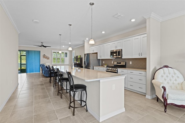 kitchen featuring ceiling fan, a kitchen island with sink, white cabinetry, appliances with stainless steel finishes, and a kitchen bar