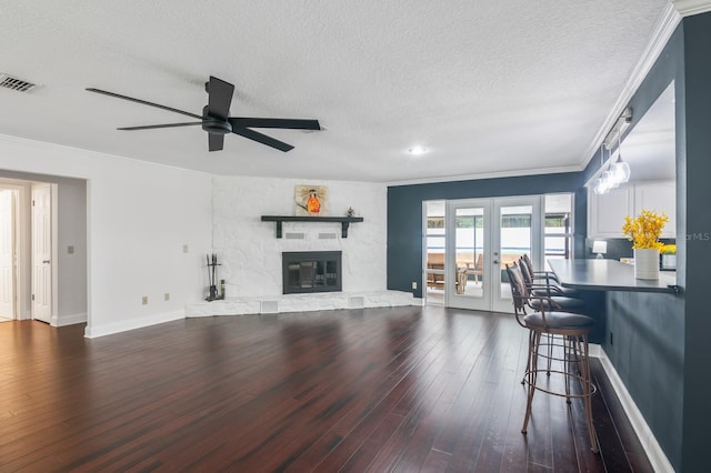 living room featuring a textured ceiling, dark wood-type flooring, a stone fireplace, ceiling fan, and french doors