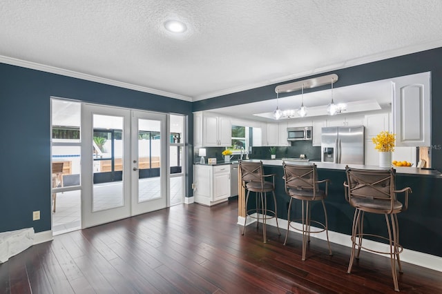 kitchen featuring white cabinets, a textured ceiling, dark wood-type flooring, appliances with stainless steel finishes, and crown molding