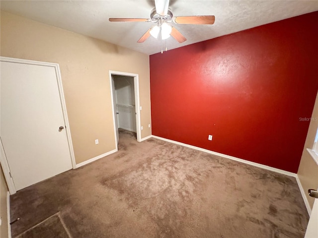 unfurnished bedroom with a ceiling fan, a walk in closet, carpet floors, a closet, and baseboards