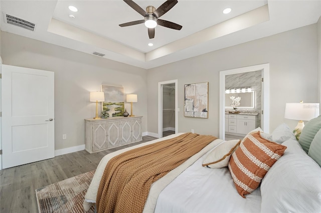 bedroom featuring a walk in closet, ensuite bath, ceiling fan, a tray ceiling, and light hardwood / wood-style floors