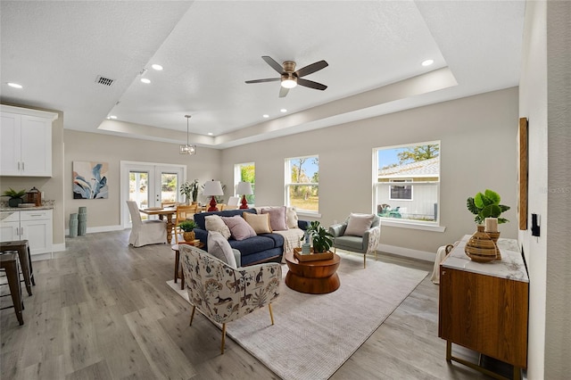 living room featuring a tray ceiling, plenty of natural light, french doors, and light wood-type flooring