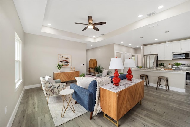 living room with a tray ceiling, ceiling fan, light hardwood / wood-style flooring, and sink