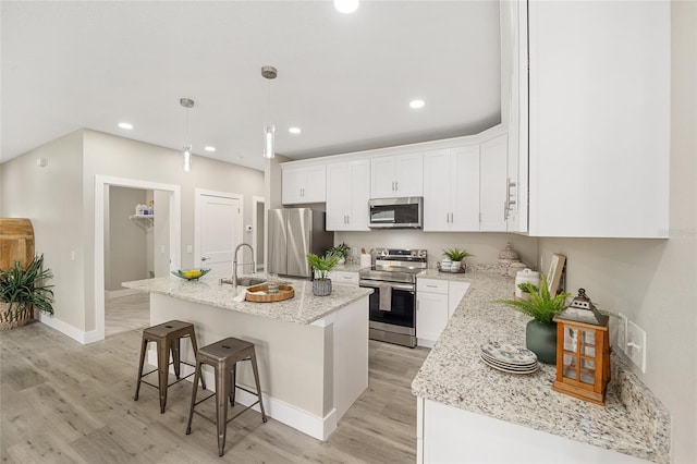 kitchen featuring white cabinetry, hanging light fixtures, a center island with sink, appliances with stainless steel finishes, and light wood-type flooring