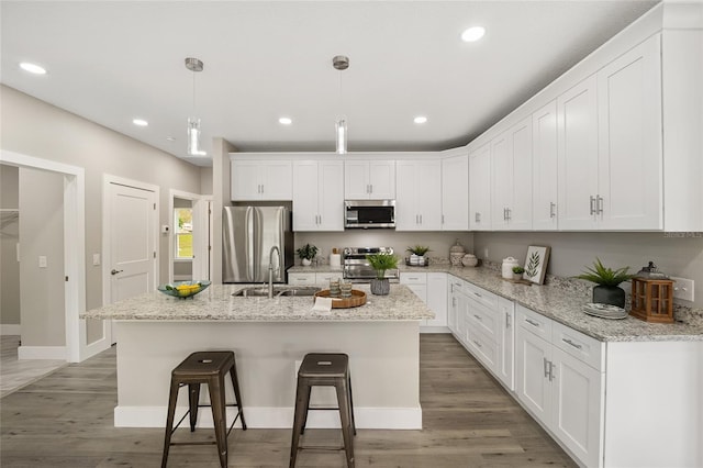 kitchen with white cabinets, a kitchen island with sink, hanging light fixtures, and appliances with stainless steel finishes