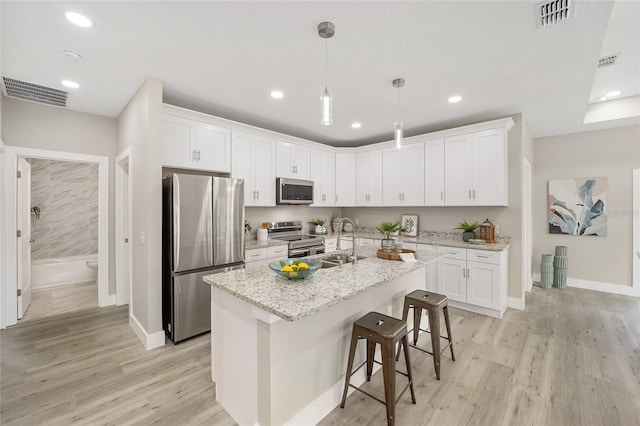 kitchen with appliances with stainless steel finishes, sink, white cabinets, hanging light fixtures, and an island with sink