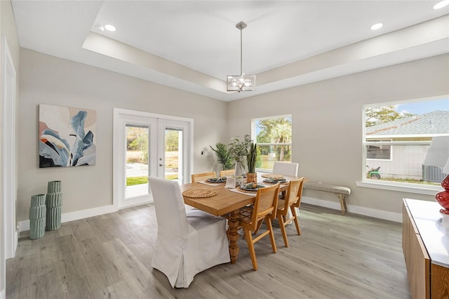 dining space featuring an inviting chandelier, light wood-type flooring, a tray ceiling, and french doors