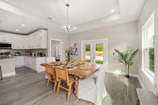 dining room with a tray ceiling, light hardwood / wood-style flooring, a chandelier, and french doors