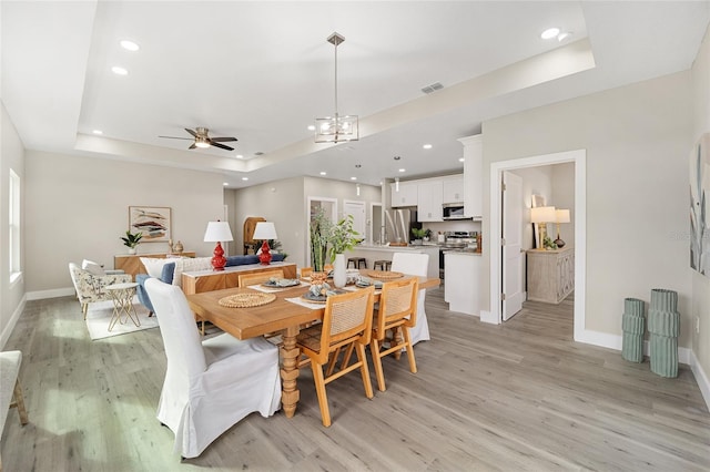 dining space with ceiling fan with notable chandelier, a raised ceiling, and light hardwood / wood-style flooring