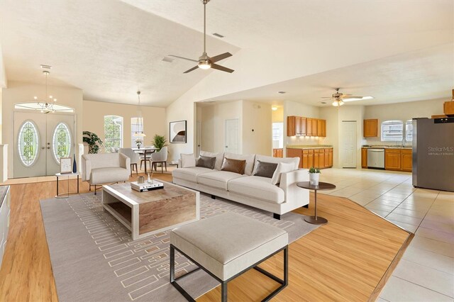 tiled living room with french doors, ceiling fan with notable chandelier, and vaulted ceiling