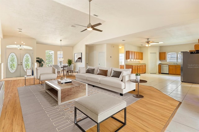 living area with lofted ceiling, ceiling fan with notable chandelier, light tile patterned flooring, and visible vents