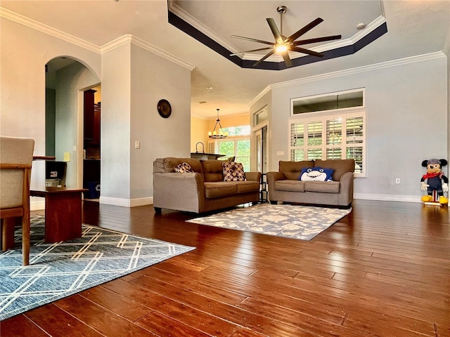 living room with ceiling fan with notable chandelier, crown molding, dark wood-type flooring, and a tray ceiling