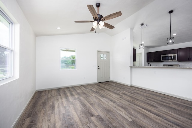 unfurnished living room featuring dark wood-type flooring, vaulted ceiling, ceiling fan, and plenty of natural light