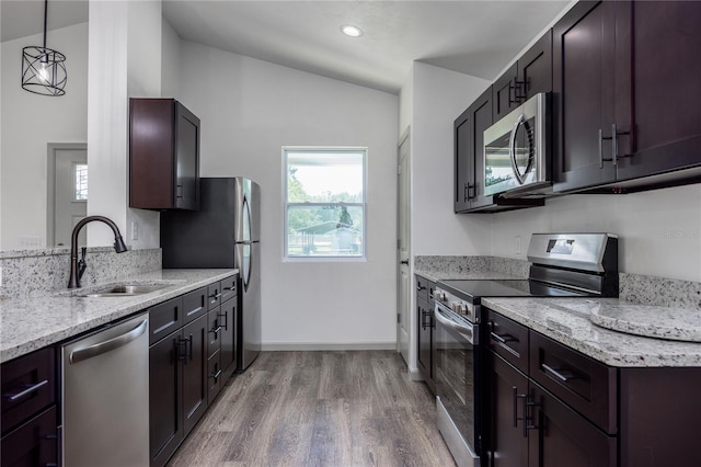 kitchen featuring lofted ceiling, light wood-type flooring, stainless steel appliances, sink, and decorative light fixtures