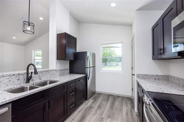 kitchen featuring lofted ceiling, stainless steel appliances, sink, light stone countertops, and light wood-type flooring