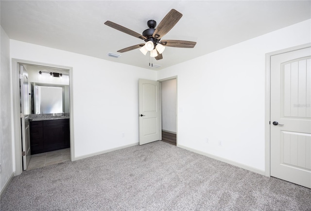 unfurnished bedroom featuring ensuite bathroom, light colored carpet, and ceiling fan