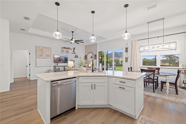 kitchen featuring light wood-type flooring, dishwasher, a kitchen island with sink, ceiling fan with notable chandelier, and white cabinets