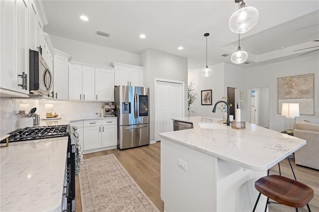 kitchen with white cabinets, an island with sink, sink, decorative light fixtures, and appliances with stainless steel finishes