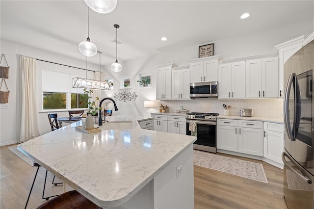 kitchen featuring pendant lighting, white cabinets, appliances with stainless steel finishes, and light hardwood / wood-style flooring