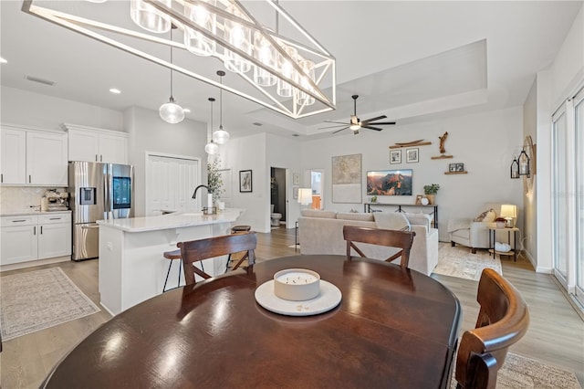 dining area featuring light hardwood / wood-style flooring, a tray ceiling, ceiling fan, and sink