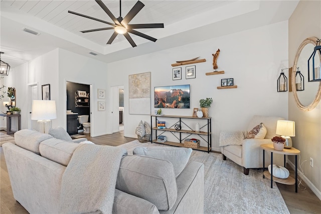 living room featuring ceiling fan with notable chandelier, light wood-type flooring, and a tray ceiling