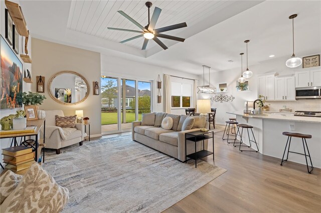 living room featuring light wood-type flooring, a tray ceiling, ceiling fan, and wooden ceiling