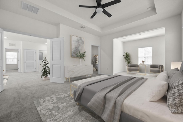 carpeted bedroom with ceiling fan and a raised ceiling