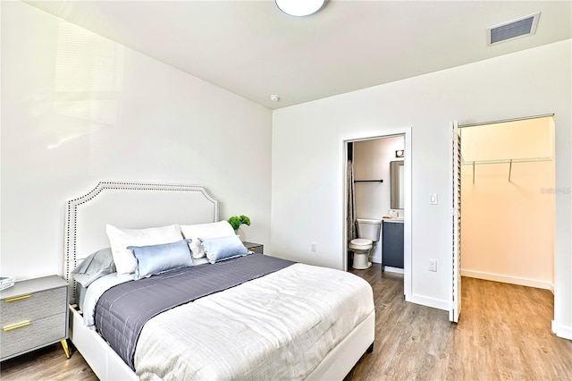 bedroom with light hardwood / wood-style floors, a walk in closet, connected bathroom, and a closet