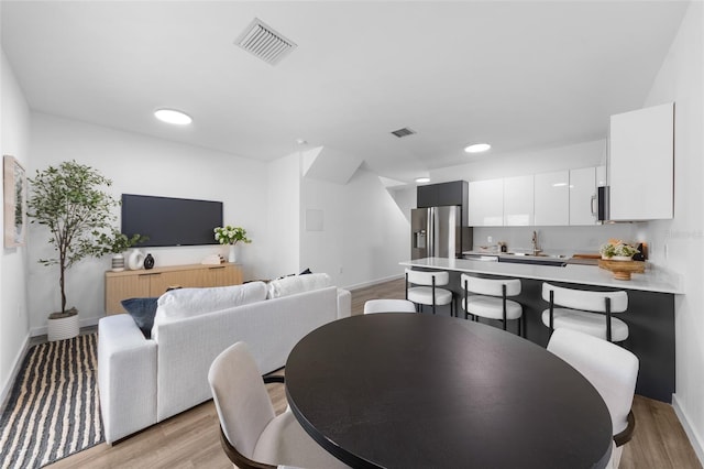 dining space with light wood-type flooring, visible vents, and baseboards