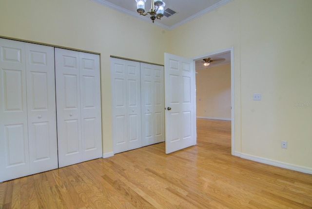 unfurnished bedroom with light hardwood / wood-style flooring, two closets, a notable chandelier, and ornamental molding