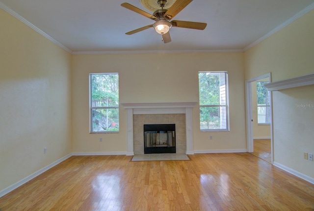 unfurnished living room featuring light wood-type flooring, a tiled fireplace, ceiling fan, and crown molding