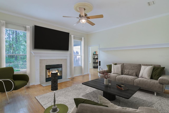 living room with a healthy amount of sunlight, a fireplace, ornamental molding, and light hardwood / wood-style flooring