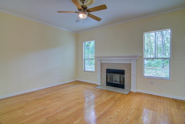 unfurnished living room featuring a tile fireplace, light hardwood / wood-style floors, ornamental molding, and ceiling fan