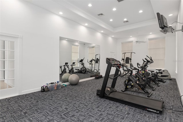 exercise room featuring a tray ceiling, ornamental molding, and dark colored carpet