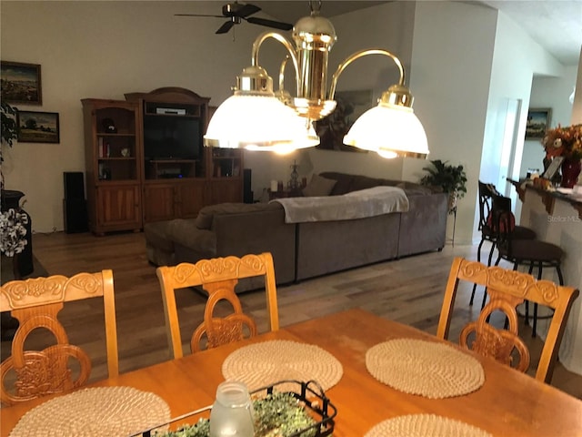 dining area with ceiling fan with notable chandelier, vaulted ceiling, and hardwood / wood-style floors