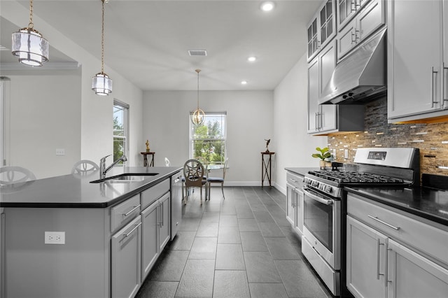 kitchen featuring tasteful backsplash, appliances with stainless steel finishes, a kitchen island with sink, sink, and decorative light fixtures