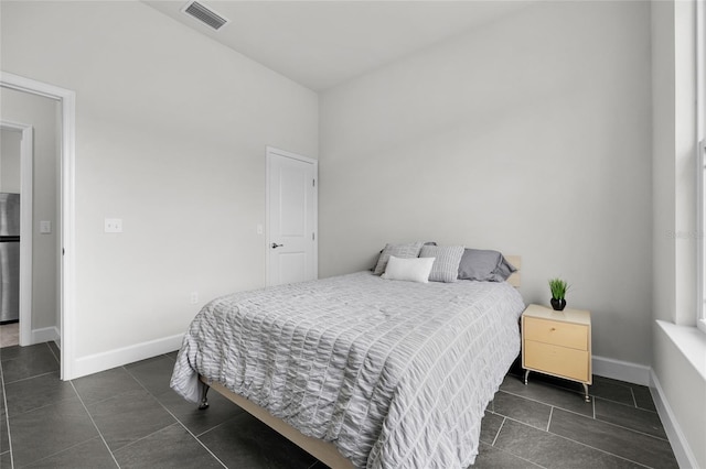 bedroom with dark tile patterned floors and stainless steel refrigerator